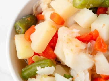 Homemade fish stew for dogs in a bowl with fresh ingredients.